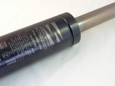 Nahaufnahme eines metallischen zylindrischen Objekts mit Aufschriften wie „SC750200D“ und „0216169“. Das Objekt scheint ein Kolben oder Stoßdämpfer zu sein. Die Oberfläche enthält verschiedene technische Spezifikationen und Symbole auf weißem Hintergrund.